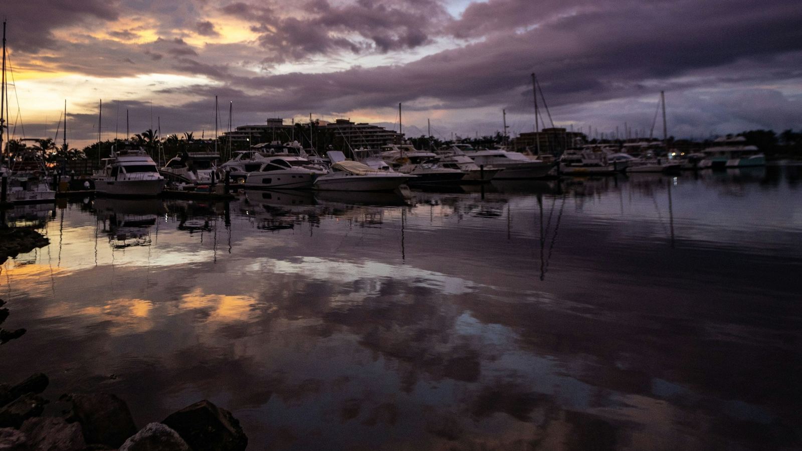 A marina at dusk, every boat tied up at its mooring under a sky of amber and violet cloud, the water perfectly still