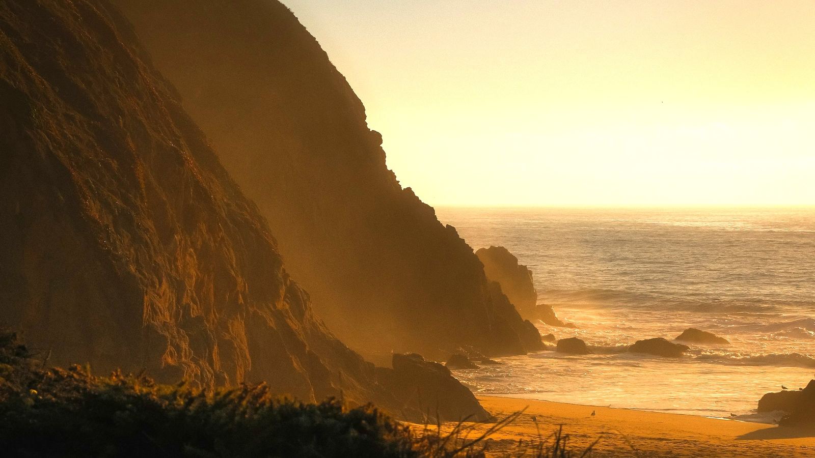 California headland at golden hour, a dark cliff turning into the open ocean, surf breaking on the rocks below