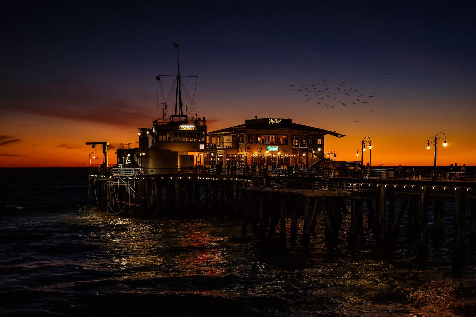 Santa Monica Pier buildings lit at dusk under an orange and deep blue sky